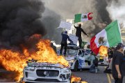 Manifestantes ondean banderas desde lo alto de un coche destrozado, junto a vehículos Waymo en llamas, mientras los manifestantes se enfrentan a las fuerzas del orden en las calles que rodean el edificio federal durante una protesta tras las operaciones federales de inmigración en Los Ángeles, California, el 8 de junio de 2025. Manifestantes incendiaron coches y se enfrentaron a las fuerzas de seguridad en Los Ángeles el 8 de junio, mientras la policía mantenía a los manifestantes alejados de las tropas de la Guardia Nacional que el presidente Donald Trump envió a las calles de la segunda ciudad más grande de EE.UU.(Foto de RINGO CHIU / AFP)