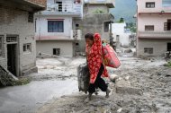 A woman salvages her belongings from her house heavily covered in mud following flash floods at Devighat in Nepals Nuwakot district on August 28, 2026. More than 1,400 people are missing and at least 552 have been killed after a devastating, tsunami-like wall of water gouged a path through the border region between Nepal and Tibet, sweeping away entire villages. (Photo by MANAN VATSYAYANA / AFP)