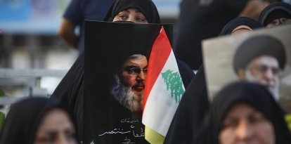 Una mujer sujeta un retrató del líder de Hezbolá Nasrallá junto a una bandera libanesa