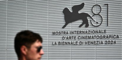 A man walks past the official logo of the 81th Venice Film Festival at Venice Lido, on August 27, 2024 on the eve of the opening ceremony. - With 21 films vying for the top Golden Lion prize, the 81st edition of the prestigious festival kicks off tomorrow, with Lady Gaga, Daniel Craig and Brad Pitt expected on the red carpet during the 10-day affair. (Photo by Marco BERTORELLO / AFP)