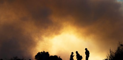 Varios bomberos observan cómo el fuego asciende por las colinas detrás de Pacific Palisades el sábado por la mañana mientras los aviones de extinción de incendios lanzan agua y rellenan para combatir las llamas