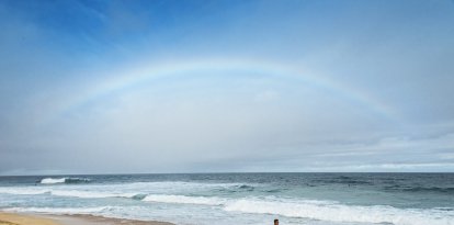 Surfistas en una playa de Hawái bajo un arcoiris.
