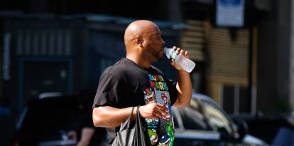 Un hombre bebe agua mientras cruza una calle en New York City, 2025.