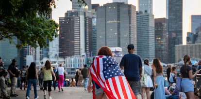 Una persona se envuelve con una bandera de Estados Unidos como una capa mientras la multitud se reúne para la celebración de los fuegos artificiales del 4 de Julio de Macy’s a lo largo del río Este