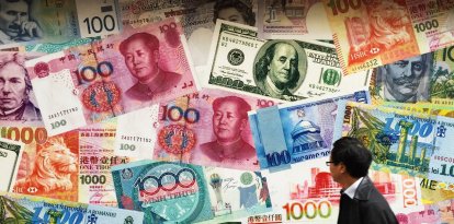 El 12 de marzo de 2015, se observa una combinación de billetes de yuan (RMB), dólar estadounidense, dólar de Hong Kong y otras divisas frente a una casa de cambio en Hong Kong. China está en conversaciones con el Fondo Monetario Internacional (FMI) para que esta institución con sede en Washington incluya el yuan en su cesta de monedas de reserva, según declaró el jueves un alto funcionario bancario, en un intento de Pekín por otorgarle un mayor protagonismo global a la moneda. El vicegobernador del banco central, Yi Gang, afirmó que China espera que el yuan se convierta en parte de los derechos especiales de giro (DEG) del FMI en un futuro próximo.