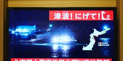 Un aviso que dice «¡Tsunami! ¡Corran!» (arriba) y «Se emite una alerta de tsunami para la costa pacífica central de Hokkaido» parpadea sobre las imágenes en directo de un barco que sale de un puerto, en una pantalla de televisión en Sapporo, en la prefectura de Hokkaido, al norte de Japón, el 8 de diciembre de 2025. Japón registró un tsunami de 40 centímetros (16 pulgadas) tras un terremoto de magnitud 7,6 el 8 de diciembre.