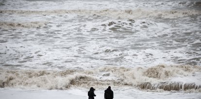 People look at the waves while standing behind a warning sign reading "Danger" (Files)