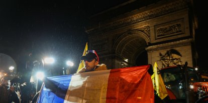 Un agricultor sostiene una bandera francesa frente al Arco del Triunfo.
