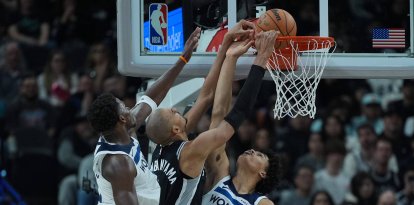 El delantero de los San Antonio Spurs, Victor Wembanyama (centro), anota contra el base de los Minnesota Timberwolves, Anthony Edwards (izquierda), y la delantera Joan Beringer (19) durante la segunda mitad de un partido de baloncesto de la NBA en San Antonio, el sábado 17 de enero de 2026.
