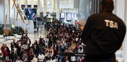 Un agente de la Administración de Seguridad del Transporte (TSA) observa a los pasajeros que hacen fila para pasar por el control de seguridad