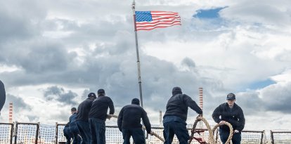 Marineros estadounidenses lanzan el cabo de amarre en la cubierta de vuelo del destructor lanzamisiles guiados de la clase Arleigh Burke USS Bainbridge (DDG 96) durante una maniobra de fondeo, el 31 de marzo de 2026.