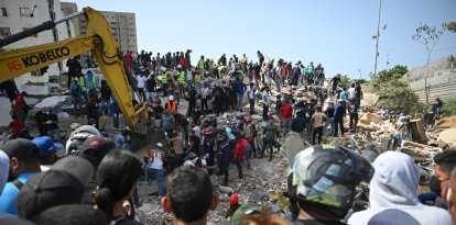 Rescatistas, voluntarios y residentes se congregan alrededor de una excavadora mientras buscan entre los escombros de los edificios derrumbados en Catia La Mar, La Guaira