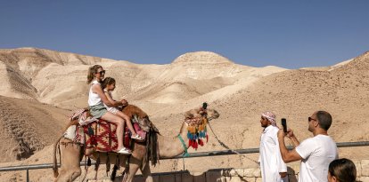 Tourists pose for a picture while riding camels near the sign marking mean sea level (Files)