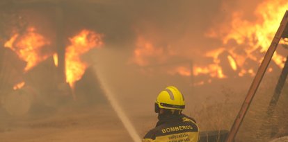 Un bombero rocía con agua neumáticos y barriles en llamas cerca de Ávila, España