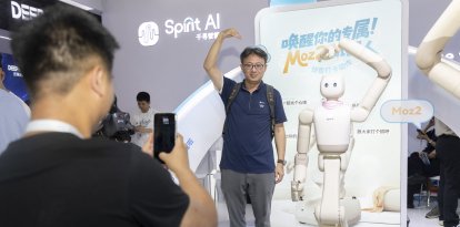 Un visitante y un robot humanoide hacen gestos de corazón mientras posan para fotos durante la Conferencia Mundial de IA 2026, en Shanghái.