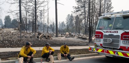 Tres miembros del Cuerpo de Bomberos de Spokane están sentados en el bordillo frente a unas viviendas calcinadas en el barrio de Balboa, en Spokane (Washington), el 2 de agosto de 2026. Los incendios, que avanzaron a gran velocidad, dejaron un rastro de destrucción el domingo en la ciudad de Spokane, situada en el noroeste de Estados Unidos; las autoridades informaron de que cientos de edificios quedaron reducidos a cenizas.