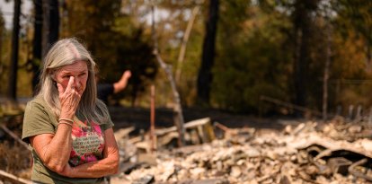 Una mujer reacciona al ver la casa de su hija calcinada durante el incendio de Old Trails en Spokane, Washington, el 4 de agosto de 2026. El martes, los equipos de emergencia se apresuraban a contener las llamas en el noroeste de EE. UU., donde un hombre fue detenido como sospechoso de incendio provocado en relación con el mayor de los incendios que han dejado sin hogar a decenas de miles de personas. Los incendios forestales, avivados por la sequía y el intenso calor, han arrasado la ciudad de Spokane, en el estado de Washington, quemando miles de acres y reduciendo a cenizas cientos de edificios, mientras las familias, angustiadas, esperan noticias sobre cuándo podrán regresar.