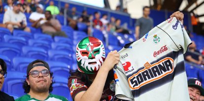 A fan of Santos Laguna wears a mask while holding up a jersey during a soccer match against Santos Laguna at Sports Illustrated Stadium in Harrison, New Jersey, on August 6, 2026. (Photo by Gordon Donovan/NurPhoto) (Photo by Gordon Donovan / NurPhoto via AFP)