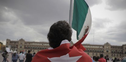 Una persona con una bandera cubana frente a la bandera de México (Archivo)