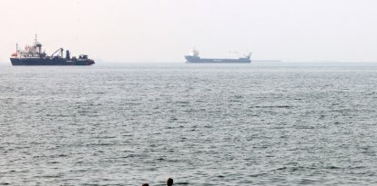 Men bathe in the Gulf waters as vessels in the background transit the Strait of Hormuz off the coast of Iran's southern port city of Bandar Abbas on September 7, 2026. Iran's top negotiator threatened on September 6 of a more forceful response to any further US attacks after Tehran targeted American warships in their latest round of clashes. The exchanges of fire, which began with US raids last week, come amid a deadlock in the six-month war between the two foes. (Photo by ATTA KENARE / AFP) /