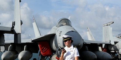 Una efectivo de la Armada estadounidense se encuentra junto a un avión en la cubierta del portaaviones USS George Washington.