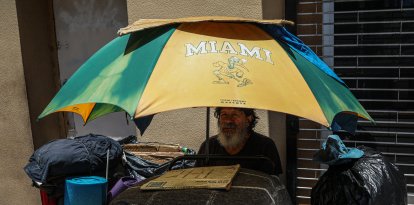 Una persona sin hogar se sienta a la sombra de una sombrilla durante una ola de calor en Miami