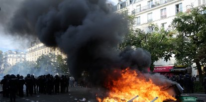 Agentes de policía custodian contenedores de basura y muebles incendiados en la calle durante una manifestación en París