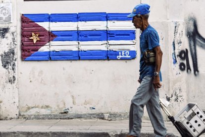 Un anciano camina frente a un mural con la bandera cubana
