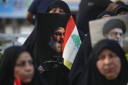 Una mujer sujeta un retrató del líder de Hezbolá Nasrallá junto a una bandera libanesa