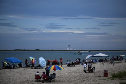 Gente sentada en la playa de South Padre Island, Texas, con la nave espacial Starship de SpaceX visible al fondo.