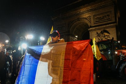 Un agricultor sostiene una bandera francesa frente al Arco del Triunfo.