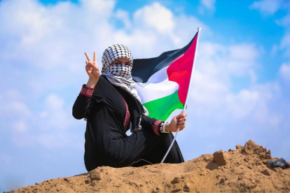 Mujer ondea la bandera de Palestina con signo de victoria.