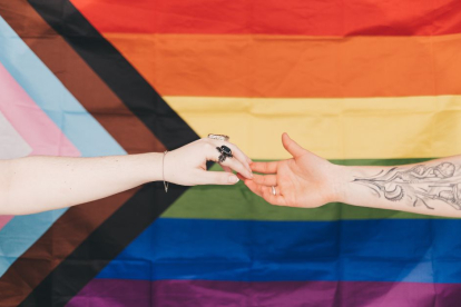 Un hombre y una mujer acercan sus manos sobre una bandera LGBT.