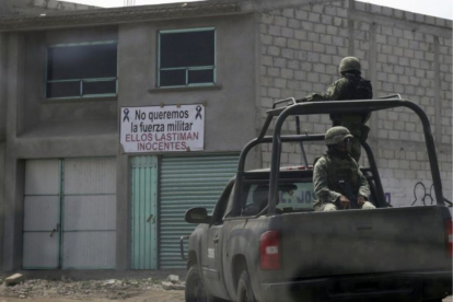Militares sobre una pick-up patrullan las calles de una localidad mexicana. Al fondo, un cartel en contra de la presencia del Ejército.