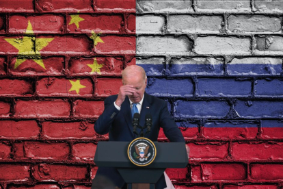 Biden sosteniéndose la cabeza delante de las banderas rusa y china.