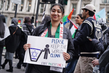 Una manifestante en Londres sostiene un cartel que muestra la bandera de Israel en un tacho de basura con un cartel que dice "por favor mantenga el mundo limpio" y "liberen a palestina.