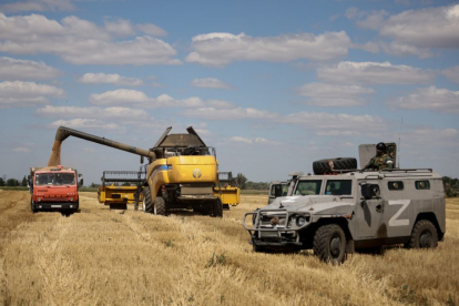 Una cosechadora echa grano en un camión en presencia de un vehículo armado en Ucrania.