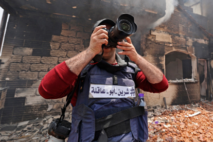 A reporter wearing a flak jacket with the hashtag in Arabic, "#Shireen Abu Akleh" takes a picture inside a house that was burnt during an Israeli military raid in the West Bank city of Jenin, on May 13, 2022. A Palestinian was wounded by Israeli fire during an operation in the northern occupied West Bank city of Jenin, Palestinian news agency Wafa said. (Photo by JAAFAR ASHTIYEH / AFP)