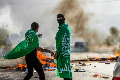 Fotografía de unos manifestantes con la bandera de Hamás, quemando neumáticos.