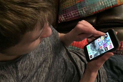 Un joven mirando su pantalla del móvil en busca de entrar en una de las redes sociales en las que tiene cuenta.
