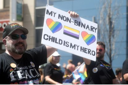 Un hombre en una marcha sostiene un cartel que reza "los niños no binarios son mis héroes".