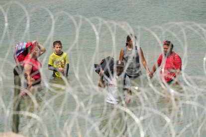 Un grupo de migrantes busca una abertura en la barrera de alambre concertina al sur de Eagle Pass