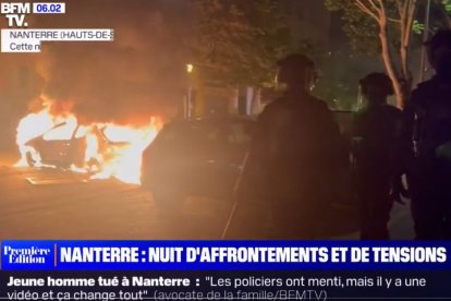 Antidisturbios franceses pasan junto a un coche ardiendo.