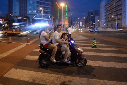 POblación en China. Una pequeña familia circula por las calles de la ciudad montada en una motocicleta de tipo scooter.