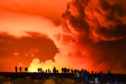 Varias personas se reúnen para observar cómo la lava fundida sale de una fisura en la península de Reykjanes, al norte de la ciudad evacuada de Grindavik, al oeste de Islandia, el 16 de marzo de 2024.