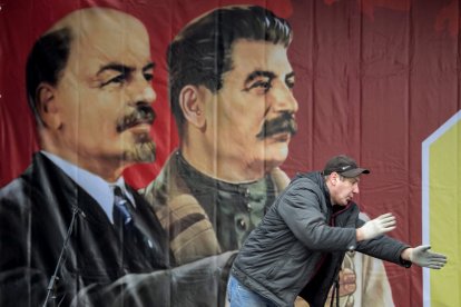 A worker gestures in front of a poster depicting Soviet leaders Vladimir Lenin and Joseph Stalin on a stage erected for events marking the 100th anniversary of The Bolshevik Revolution in downtown Moscow on November 7, 2017. (Photo by Mladen ANTONOV / AFP)
