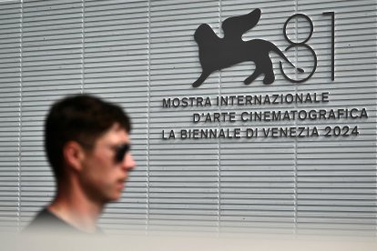 A man walks past the official logo of the 81th Venice Film Festival at Venice Lido, on August 27, 2024 on the eve of the opening ceremony. - With 21 films vying for the top Golden Lion prize, the 81st edition of the prestigious festival kicks off tomorrow, with Lady Gaga, Daniel Craig and Brad Pitt expected on the red carpet during the 10-day affair. (Photo by Marco BERTORELLO / AFP)