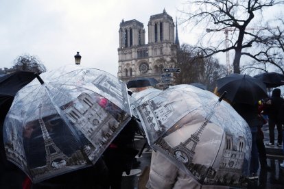 Personas desafían la lluvia bajo paraguas miran la catedral de Notre-Dame el día después de la reapertura de la emblemática catedral, en el centro de París, el 8 de diciembre de 2024.