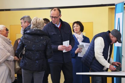 Friedrich Merz (CDU, centro), presidente del partido y candidato a canciller, habla con un ciudadano mientras deposita su voto junto a su esposa Charlotte Merz (2ª por la derecha) en el colegio electoral de Schützenhalle Arnsberg-Niedereimer.