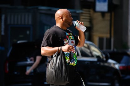Un hombre bebe agua mientras cruza una calle en New York City, 2025.